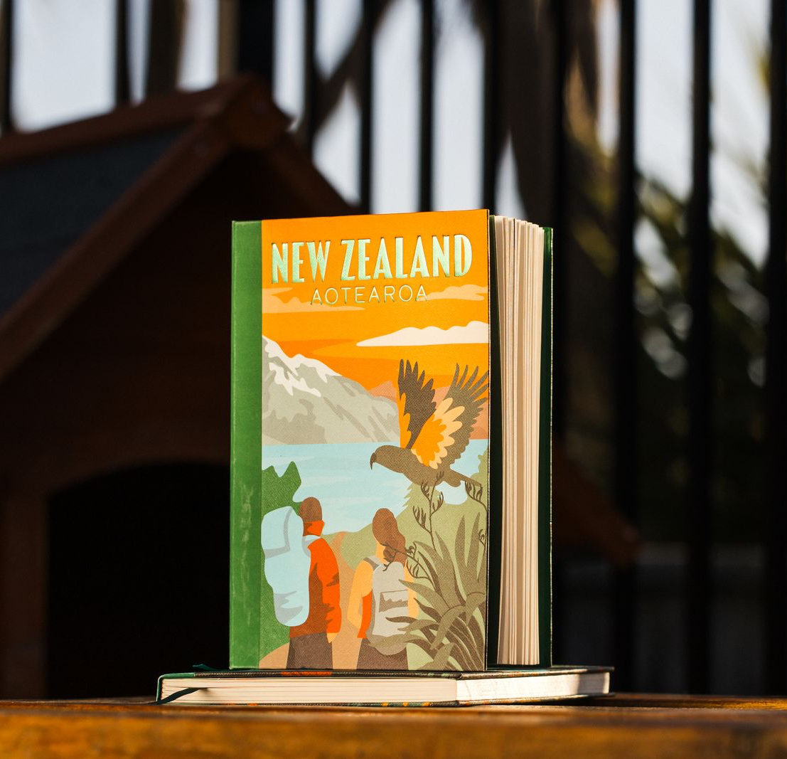 Notebook with New Zealand hiking design and a Kea bird cover placed on a wooden desktop.