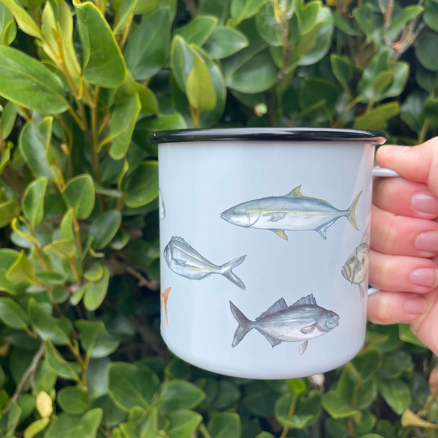 Enamel mug in pale blue with fish decals on it.