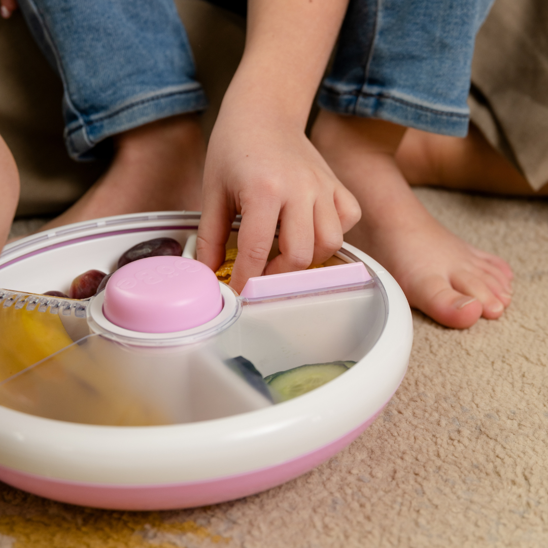 Childs hands reaching into a Gobe snack spinner lunch box in light purple & white..
