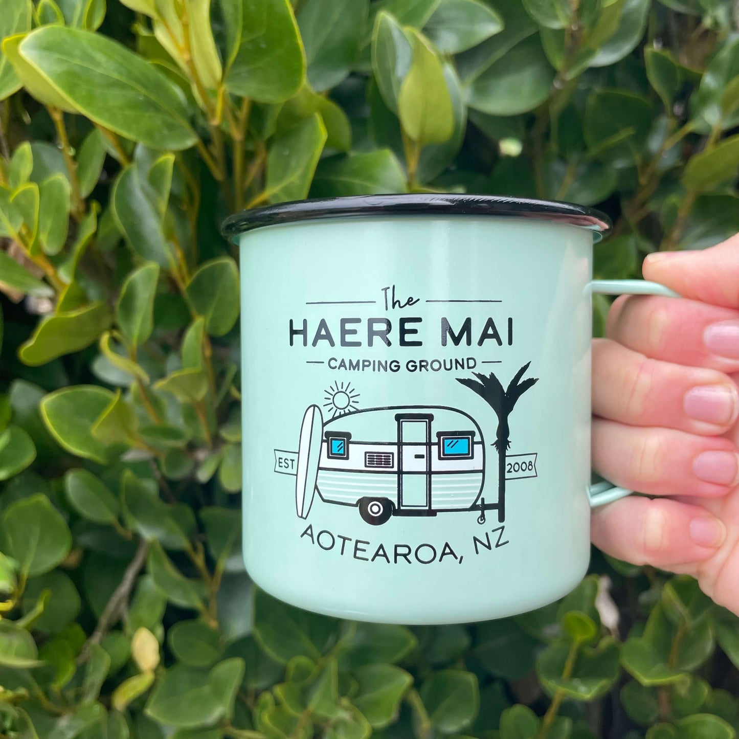 Mint green Haere Mai camping ground enamel mug with a caravan image on it.