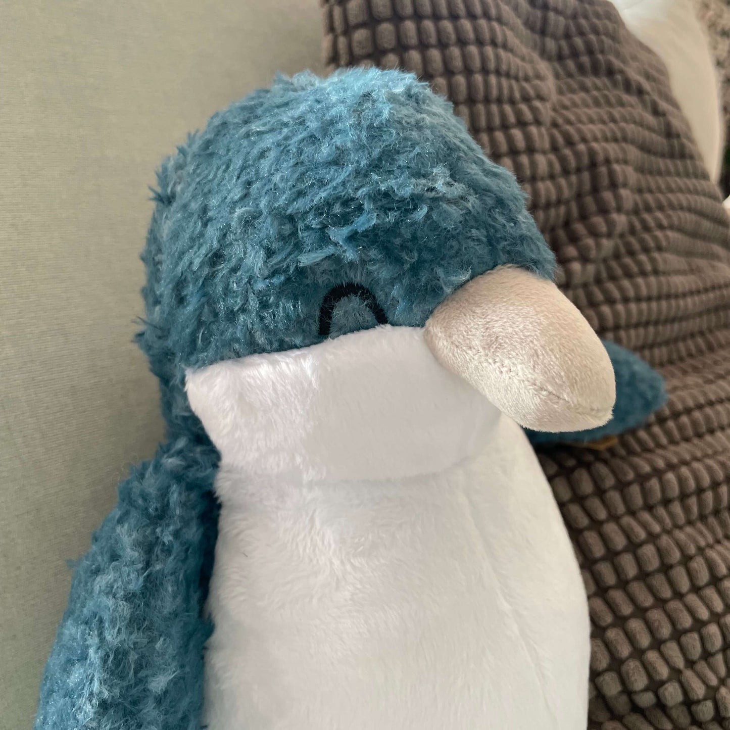 Close up of a soft toy Little Blue Penguins face. It has a blue head with closed black embroidered eye and a pale pink beak and a white tummy.