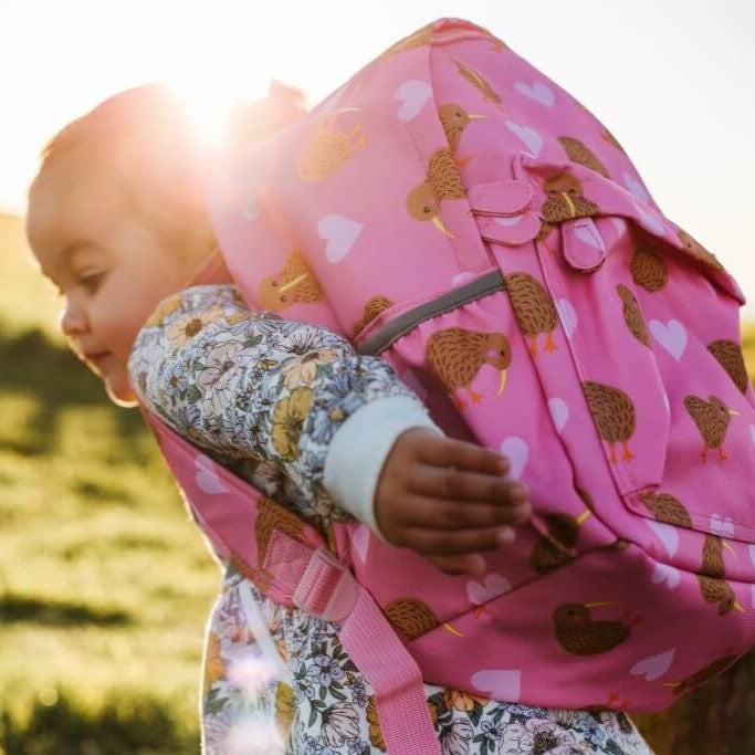 A young girl wearing a pink kids backpack with lighter pink hearts and brown kiwi birds print.