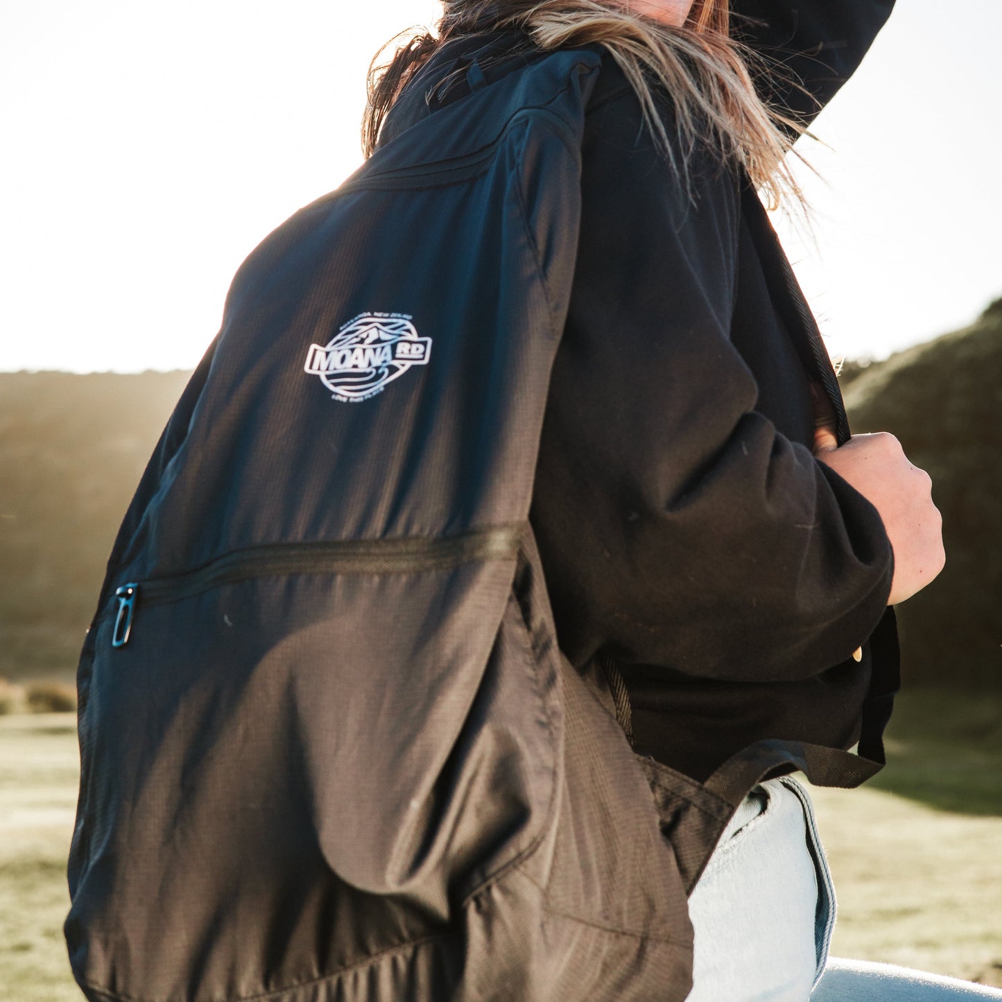 Woman wearing a Lightweight black backpack with front pocket and Moana RD logo in white over her right shoulder.