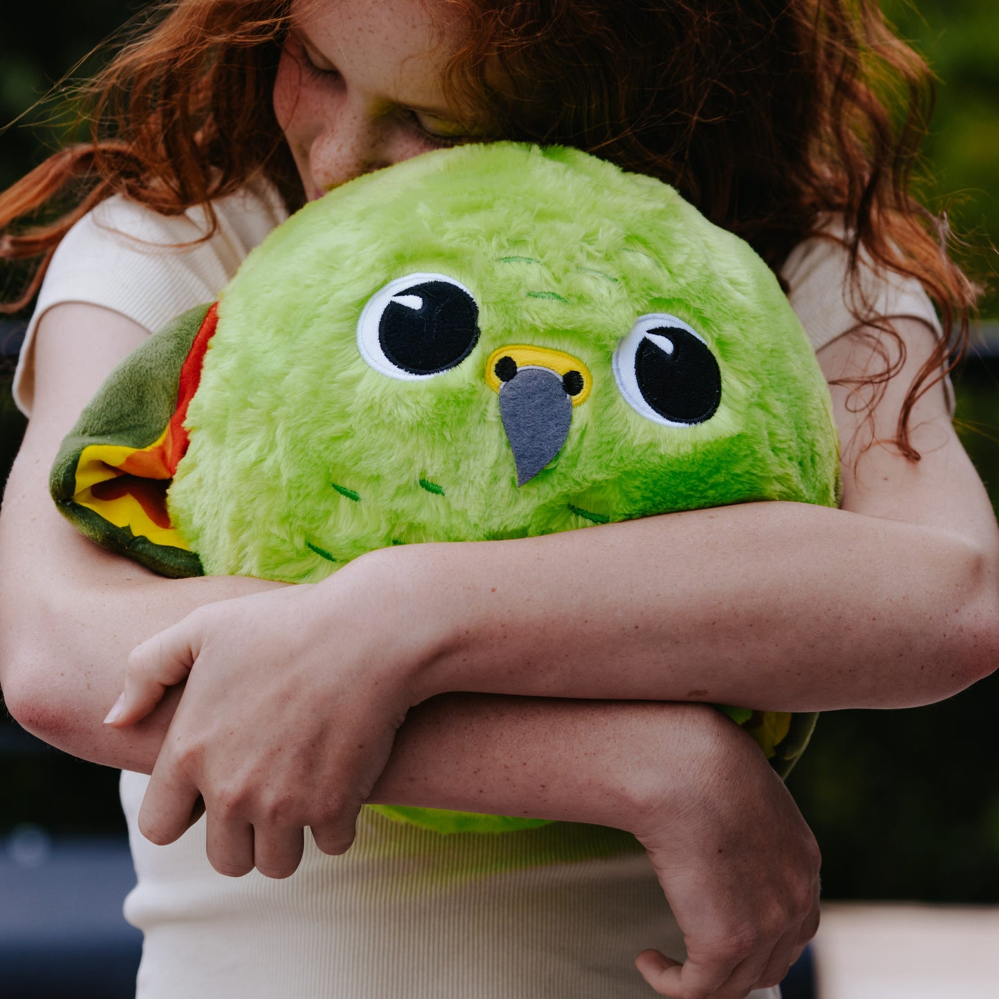 Young girl with long red hair hugging a green inflatable plush Kea bird ball.