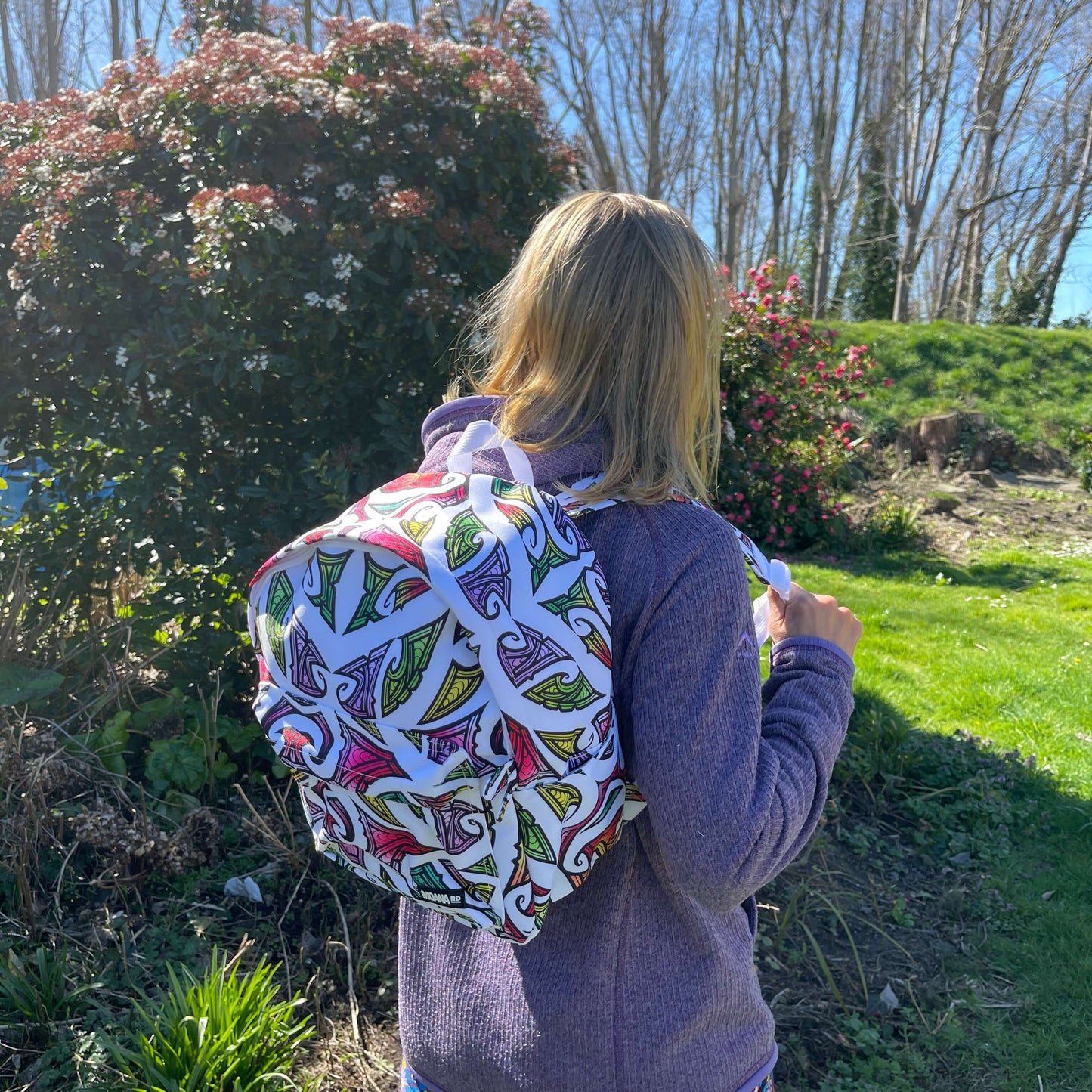 Teenager wearing a kids backpack in white with colourful Maori design by Miriama Grace Smith.