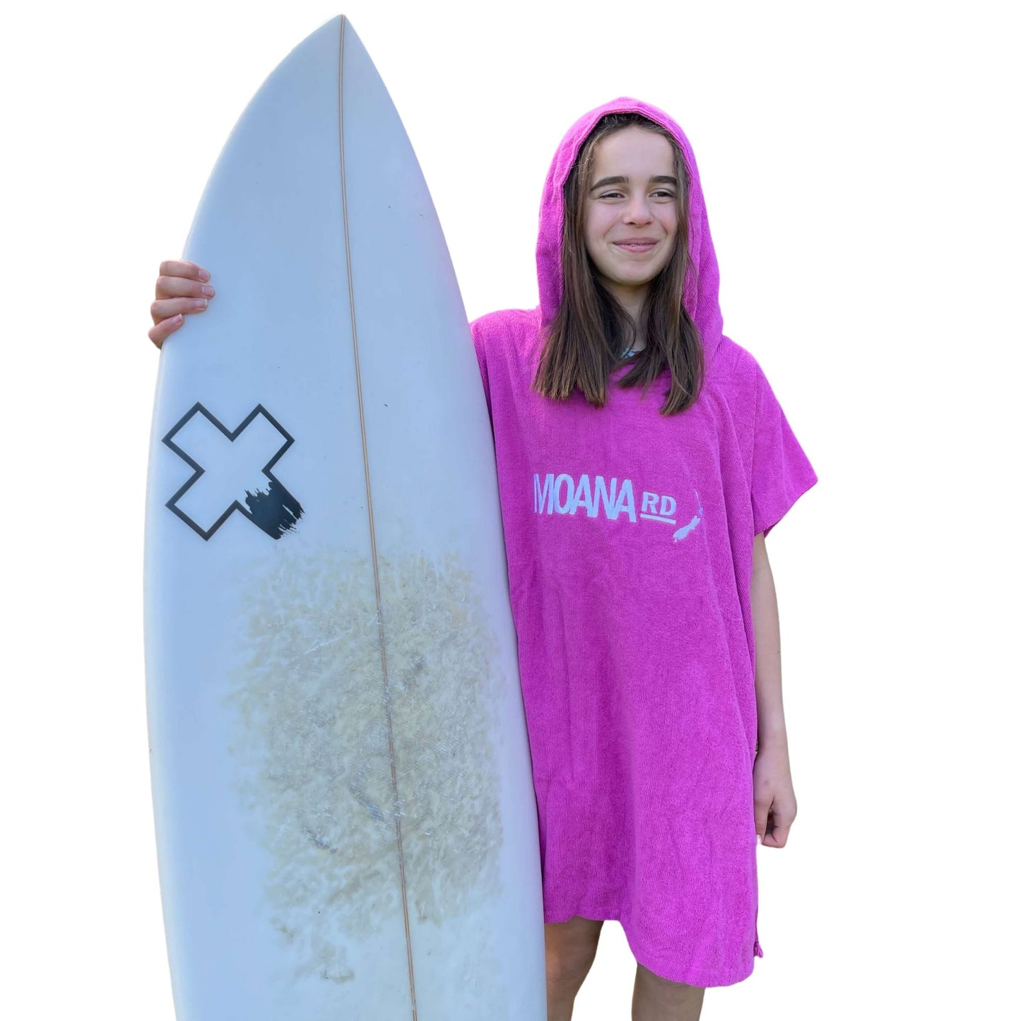 Young girl wearing a bright pink towel hoodie with the words Moana RD on it in white and a map of New Zealand. She is holding a surfboard.