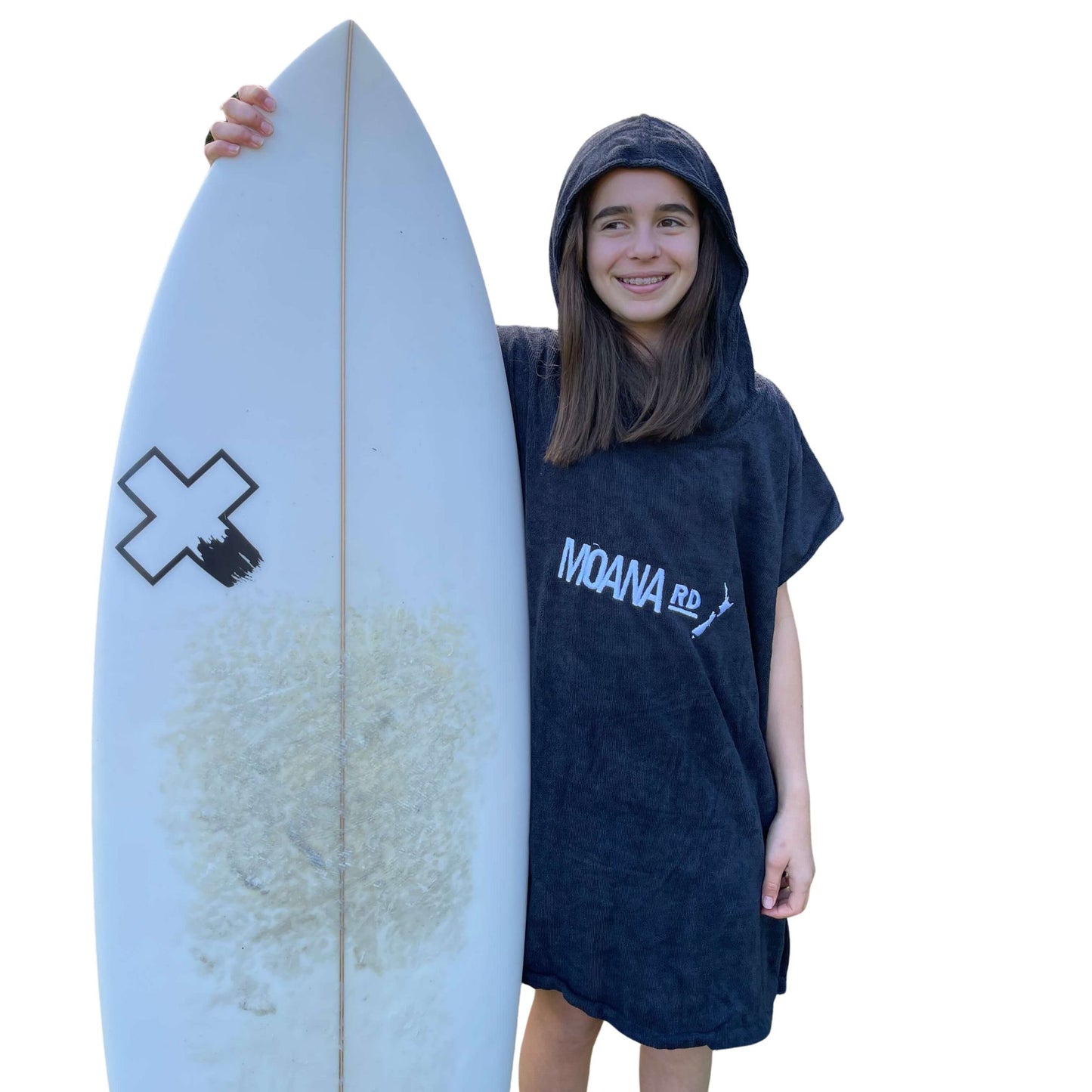 Young girl wearing a black towel hoodie with the words Moana RD on it in white and a map of New Zealand. She is holding a surfboard.