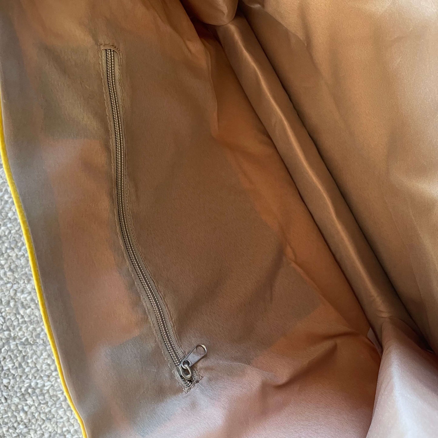 Close up of the interior zip pocket in light brown lining fabric inside a yellow tote bag.