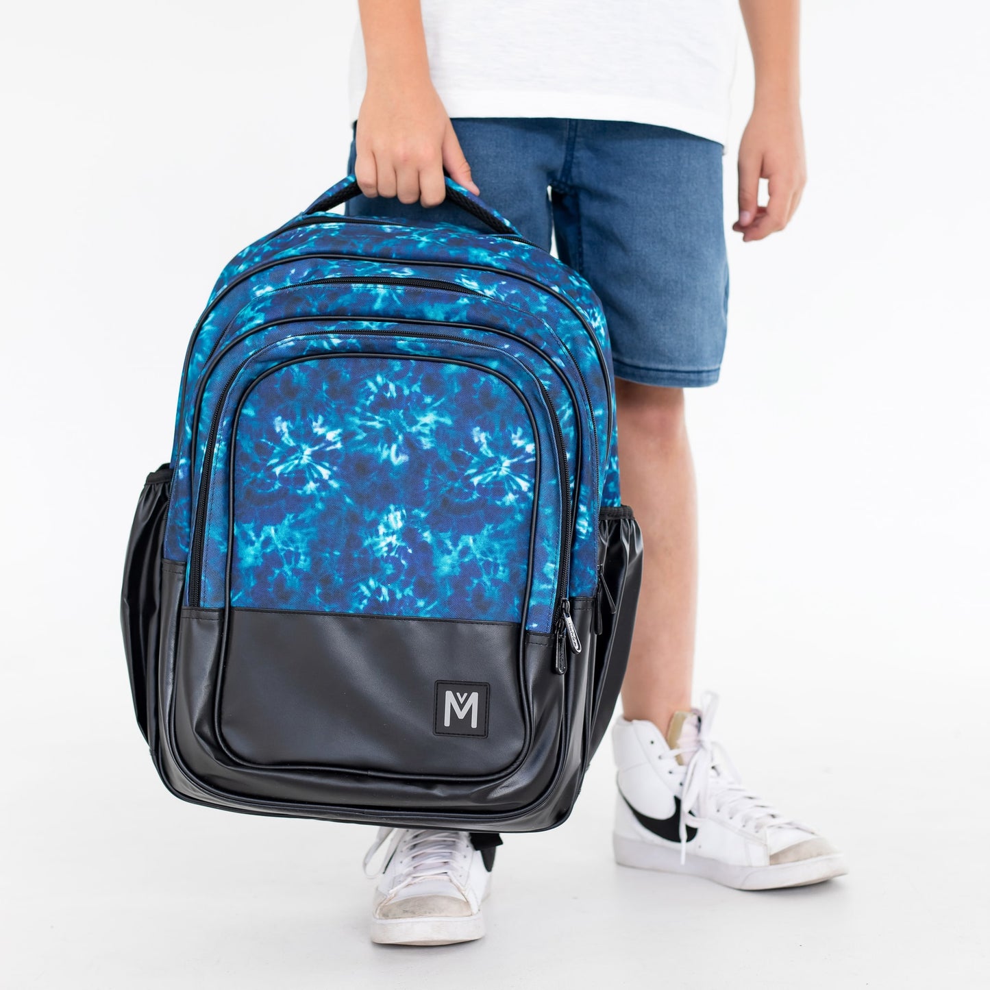Child holding the top loop handle of a blue and black Montiico backpack.