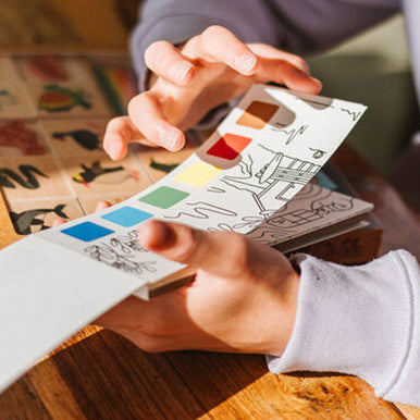 Person holding a watercolour painting notepad in their hands.