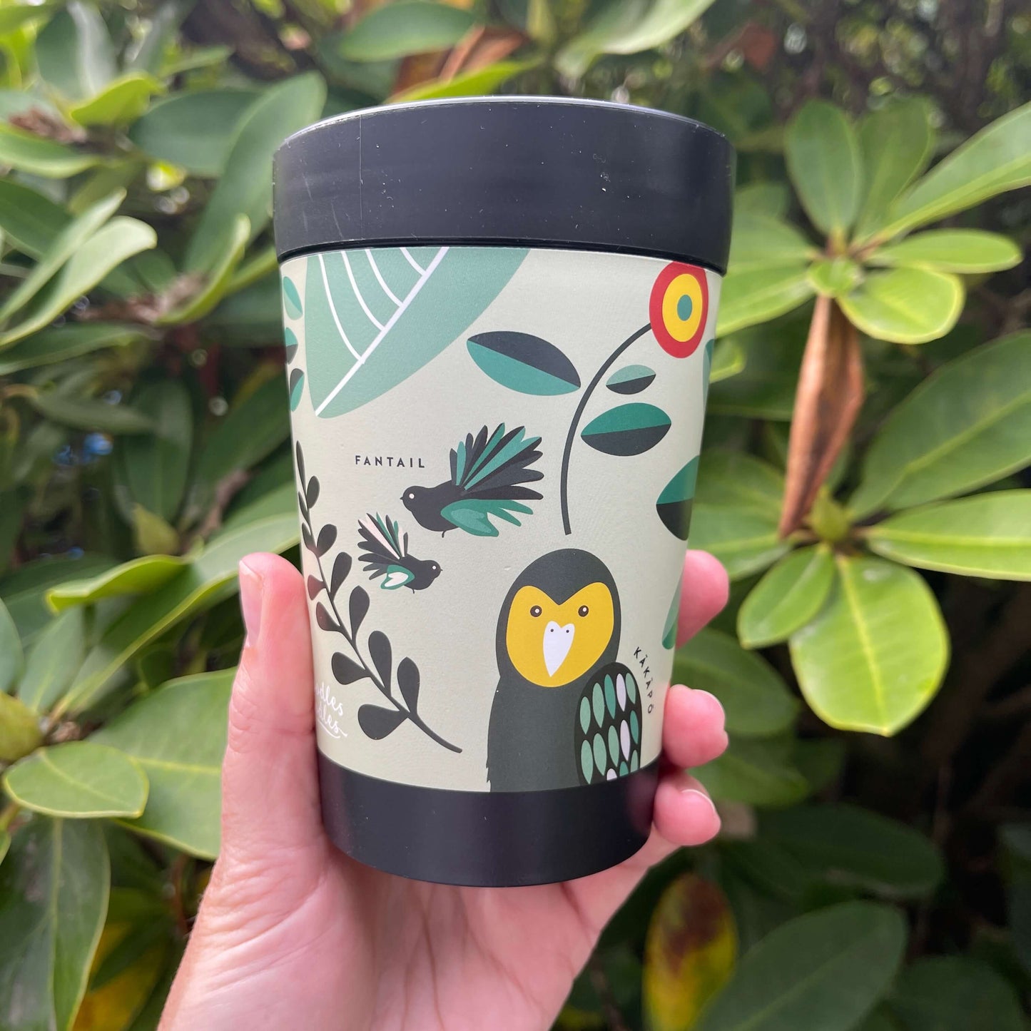 Black reusable coffee cup featuring New Zealand birds in a cartoon style on a minty green wrap background.