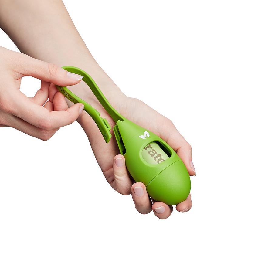 Bright green silicone tea drop shaped dog poo bag dispenser with women's hands showing how the loop is removed to attach to a leash.