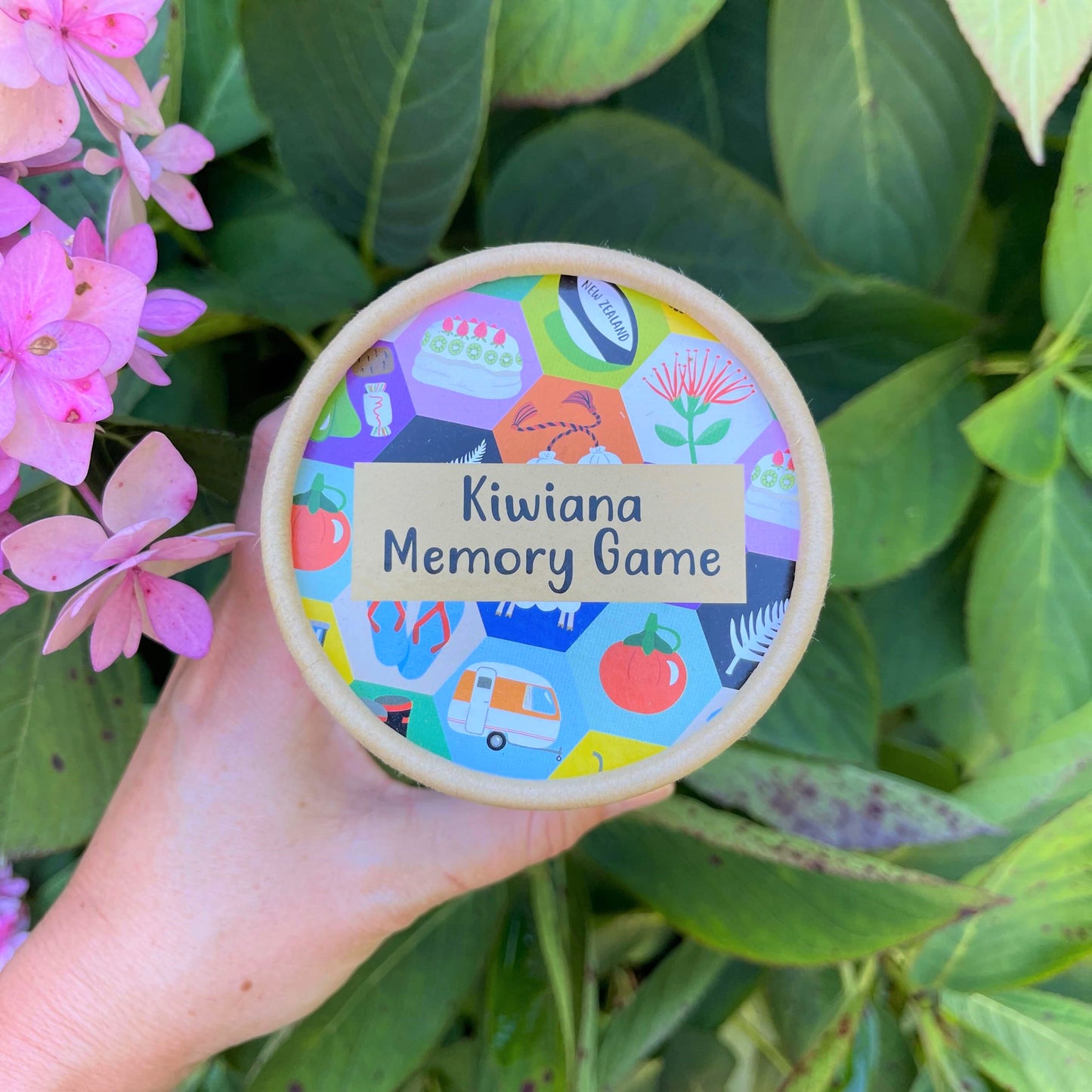 Women's hand holding cardboard tube with a Kiwiana Memory Game inside.