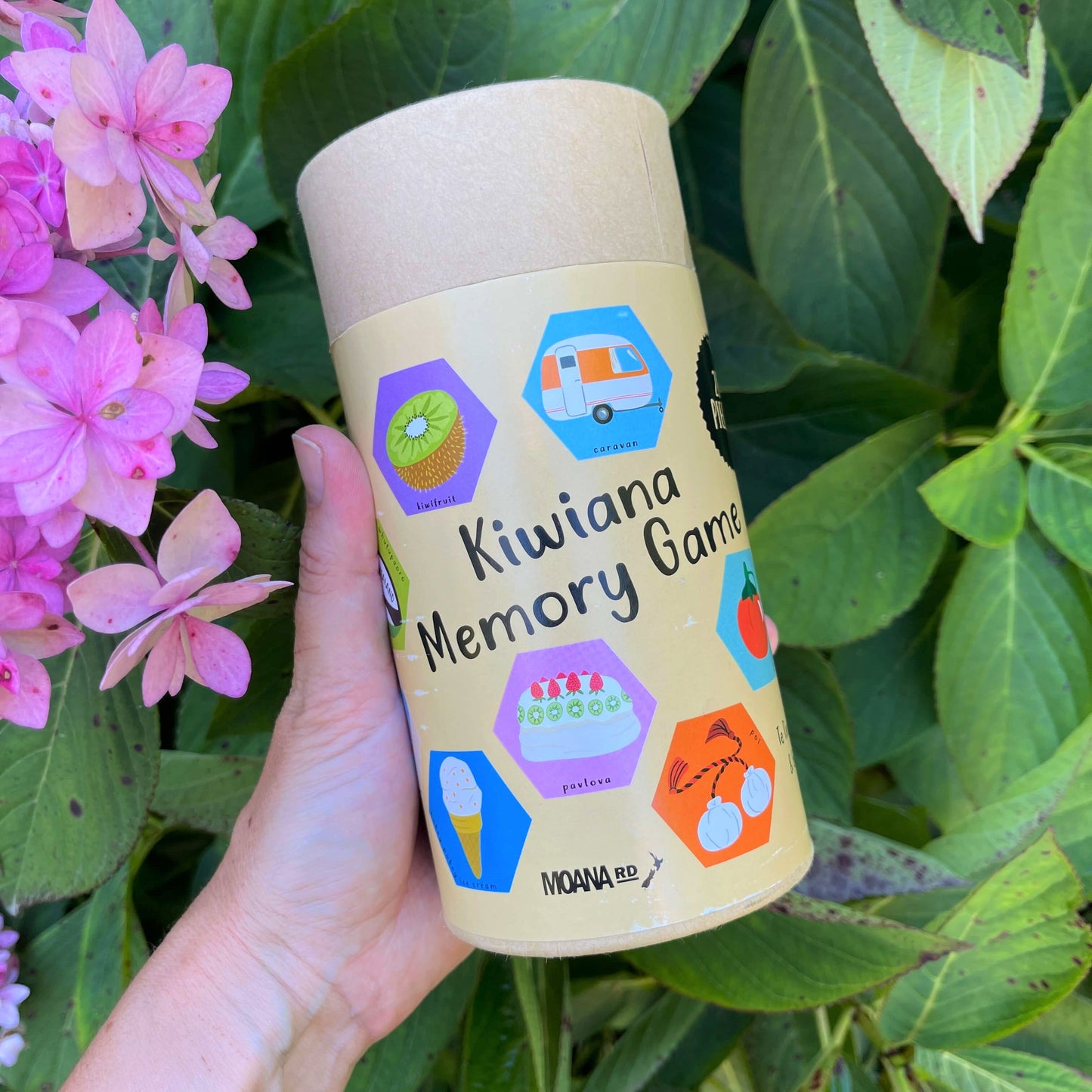 Women's hand holding cardboard tube with a Kiwiana Memory Game inside.