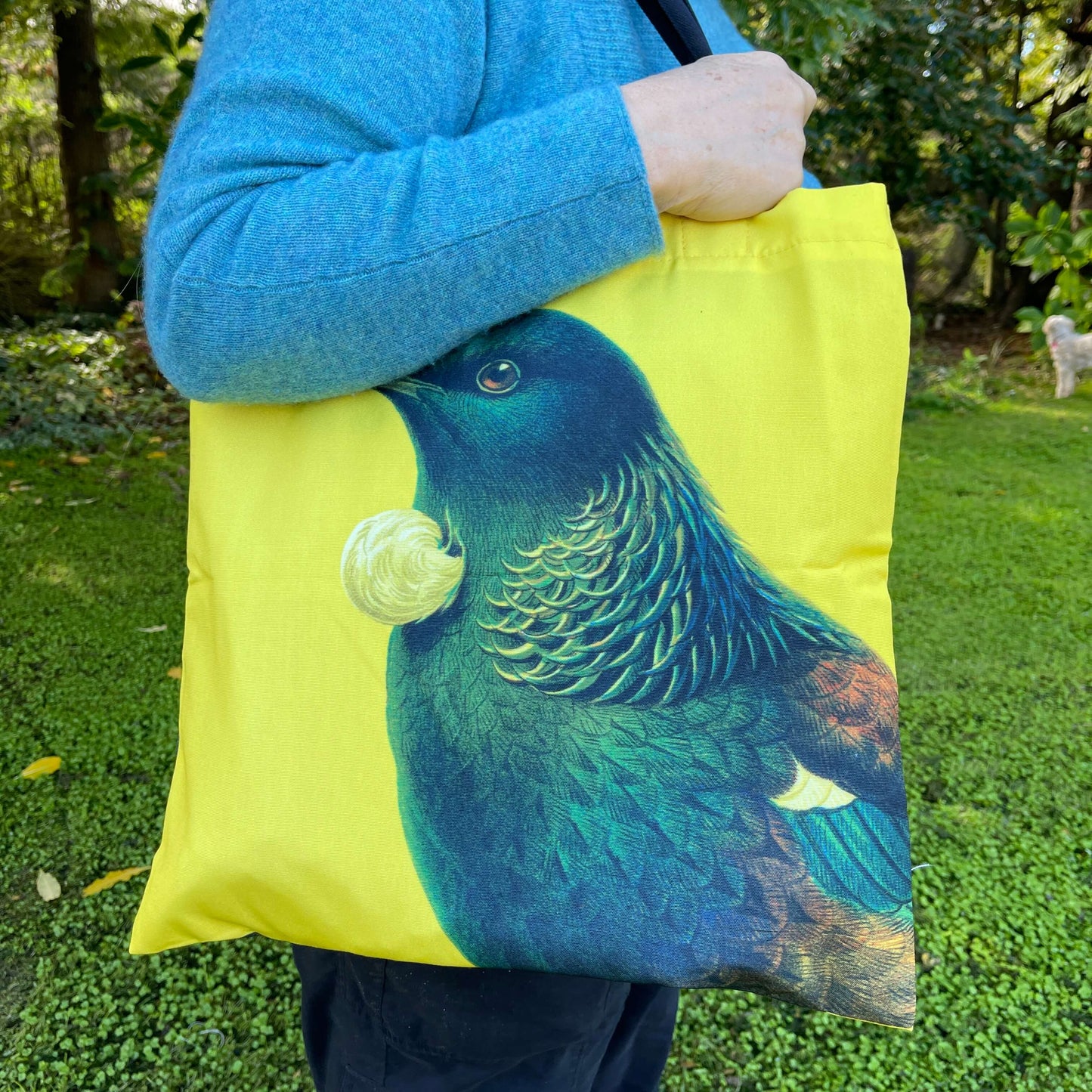 Woman with a tote bag over her arm. The bright yellow tote features a Tui bird.