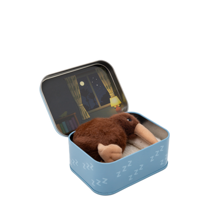 A small brown plush sleeping kiwi bird toy nestled inside an open light blue tin with a night-themed illustration on the lid, shown on a plain white background.