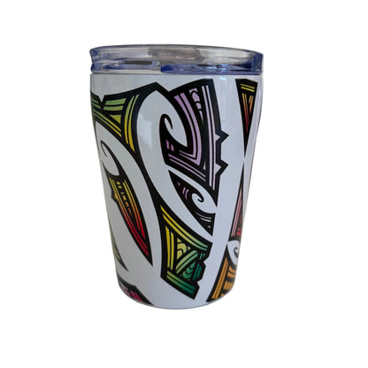 A white insulated stainless tumbler with a clear lid, decorated with a bold black tribal-style graphic pattern featuring green, yellow, red, and purple details.