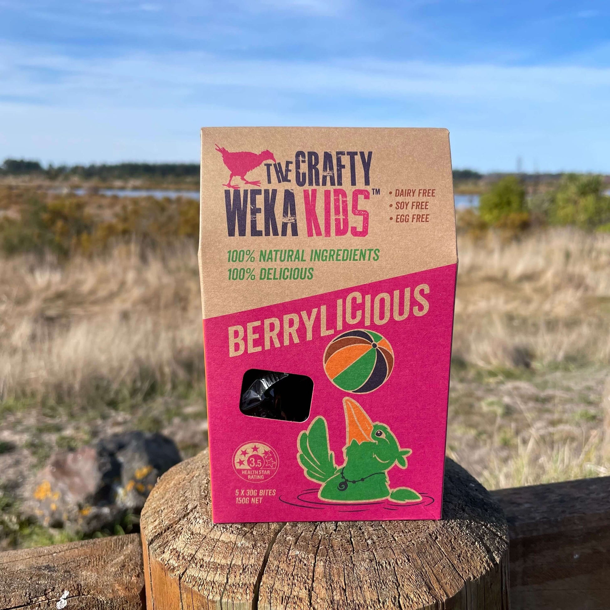 Cardboard pouch of berrylicious muesli bars from Crafty Weka sitting on a fence post overlooking an Estuary.