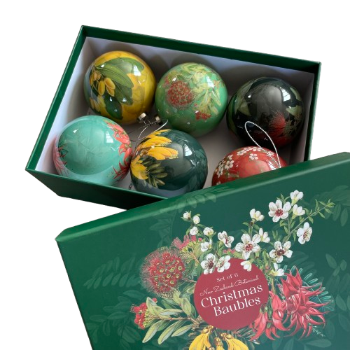 Dark green rectangle box with the lid leant up against it. On the lid is a spray of native NZ flowers with the words Set of 6 New Zealand Botanical Christmas Baubles. In the box are 6 Christmas baubles each with a different native floral picture and colour scheme.