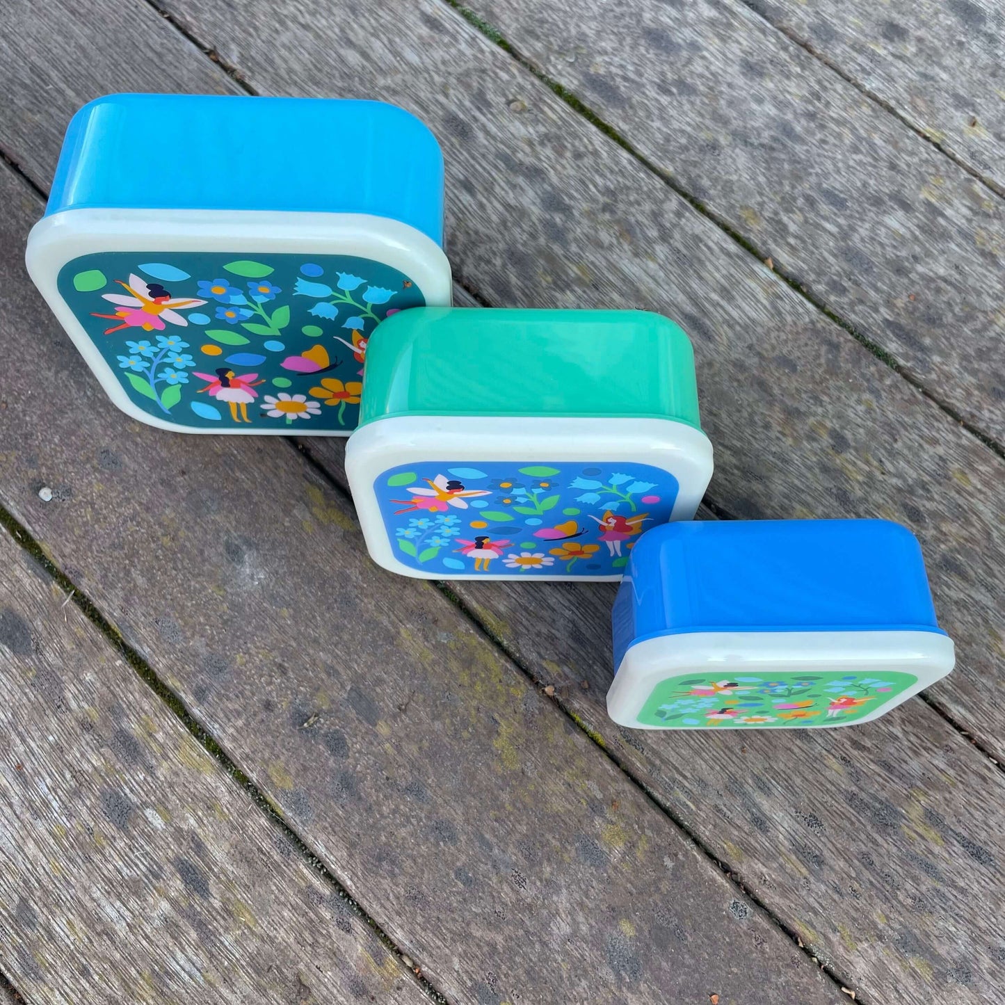 Set of 3 snack boxes in shades of blue and green with a fairy garden print on each lid.