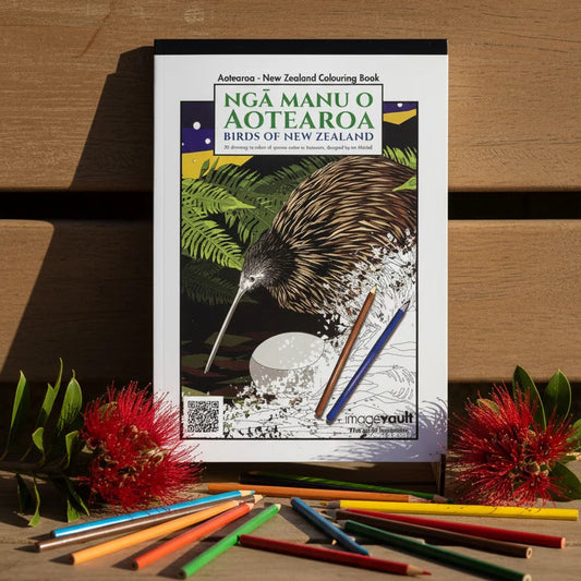A coloring book titled 'Nga Manu o Aotearoa Birds of New Zealand' is displayed on a wooden surface with colored pencils and red flowers around it. The cover features an illustration of a kiwi bird.