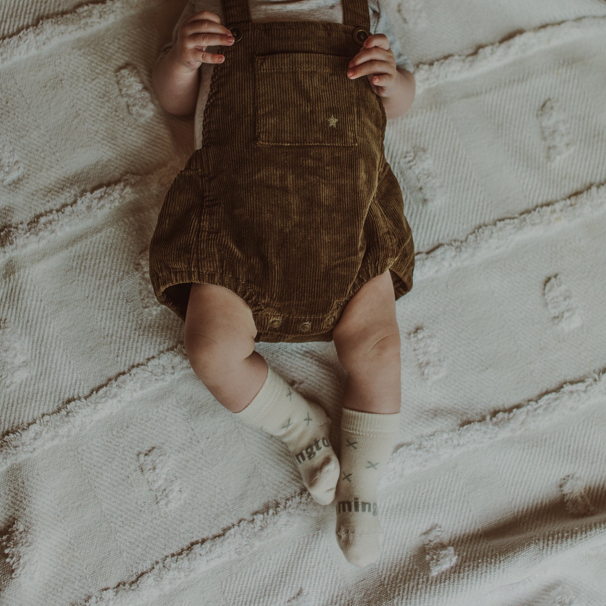 Baby wearing a brown corduroy romper and cream merino socks with grey X print.