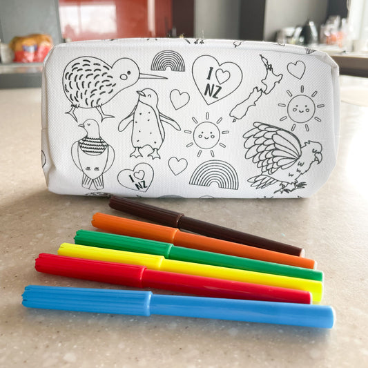 White pencil case with black outlines of New Zealand birds and other icons with 6 felt tip pens sitting on the bench in front of it.