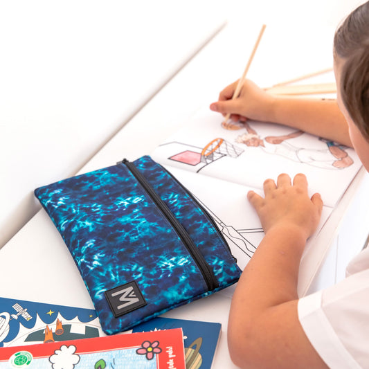 Child drawing on paper with a blue tie dye print pencil case as the feature.