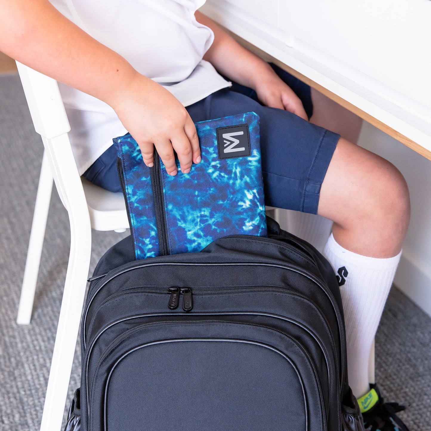 Childs hands pulling a blue tie dye pencil case from a black backpack.