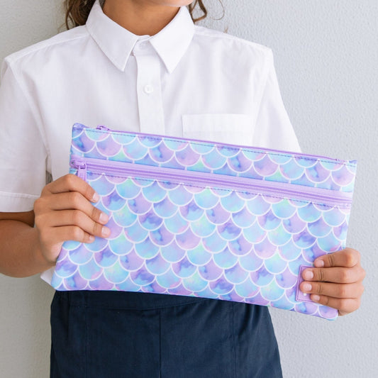 Close up of a childs hands holding onto a purple and blue mermaid scale print pencil case.