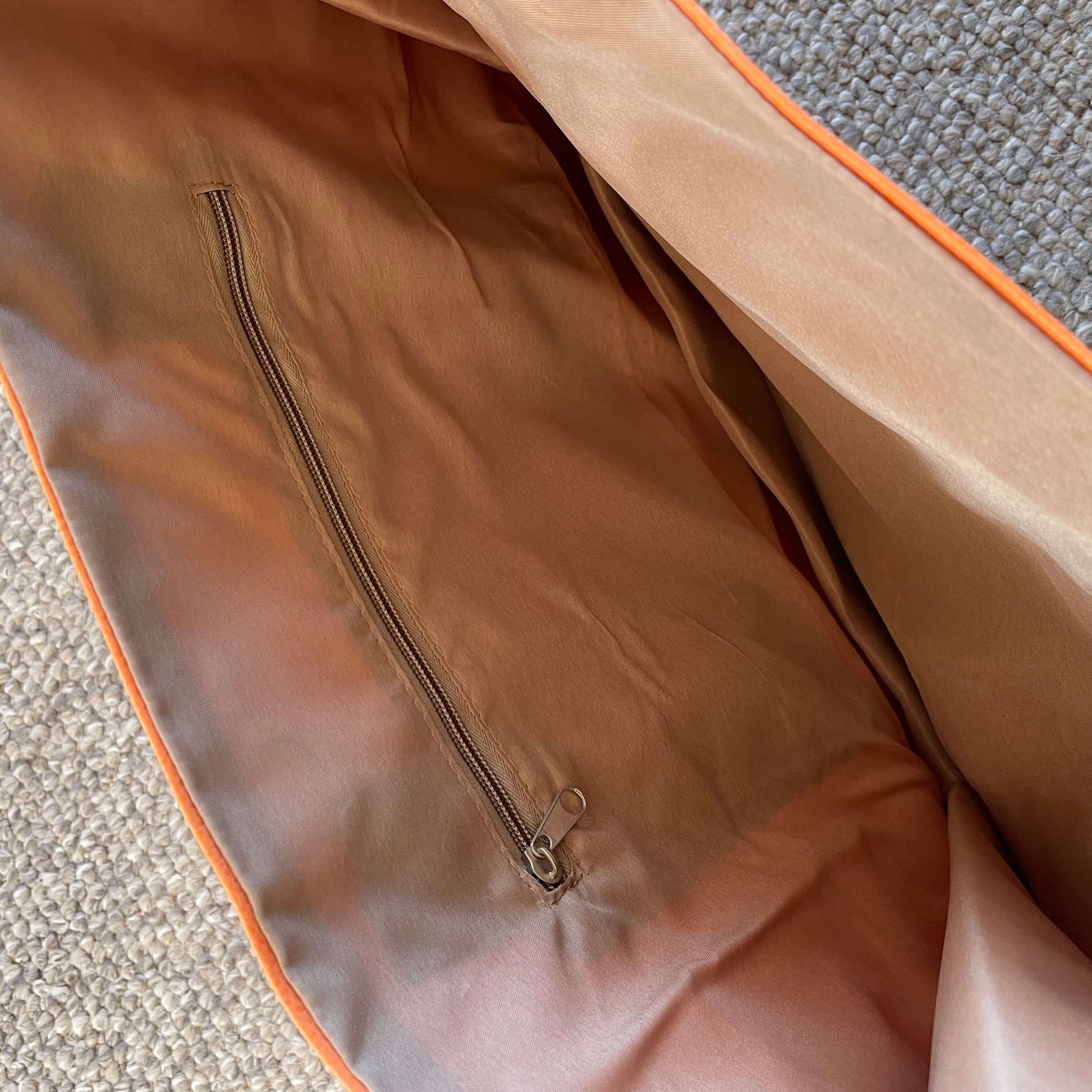 Close up of the interior zip pocket  in light brown lining fabric inside an orange tote bag.