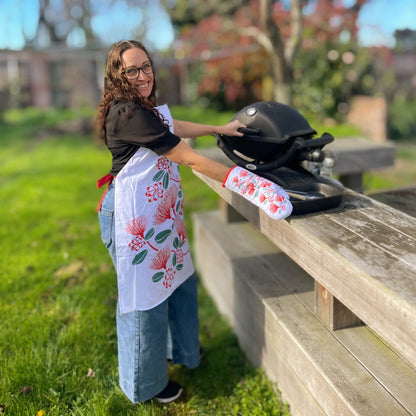 Women wearing a white apron with red and green pohutukawa flower print at a BBQ.