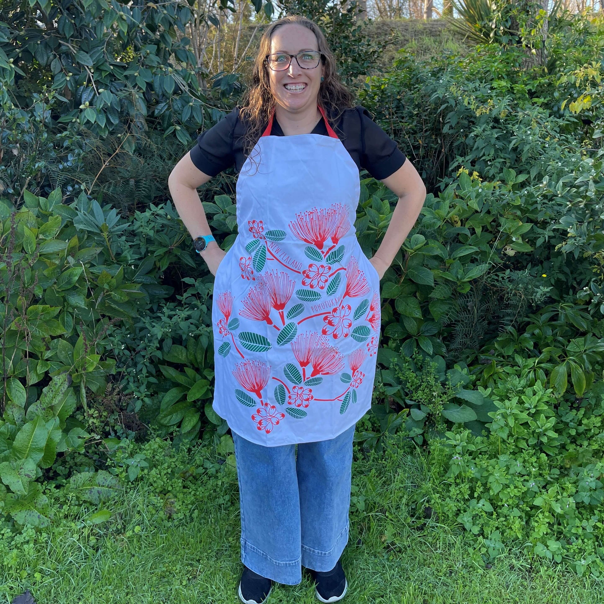 Women wearing a white apron with red and green pohutukawa flower print.