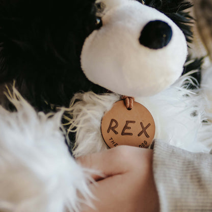Close up of the face of a black and white soft toy sheep dog. The toy dog has a brown leather name tag with REX on it.