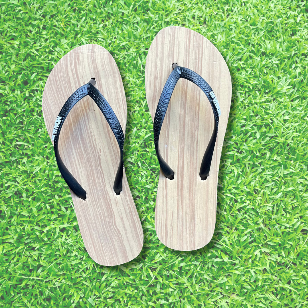 A pair of woodgrain look slim fit jandals with black straps placed on a grassy background.