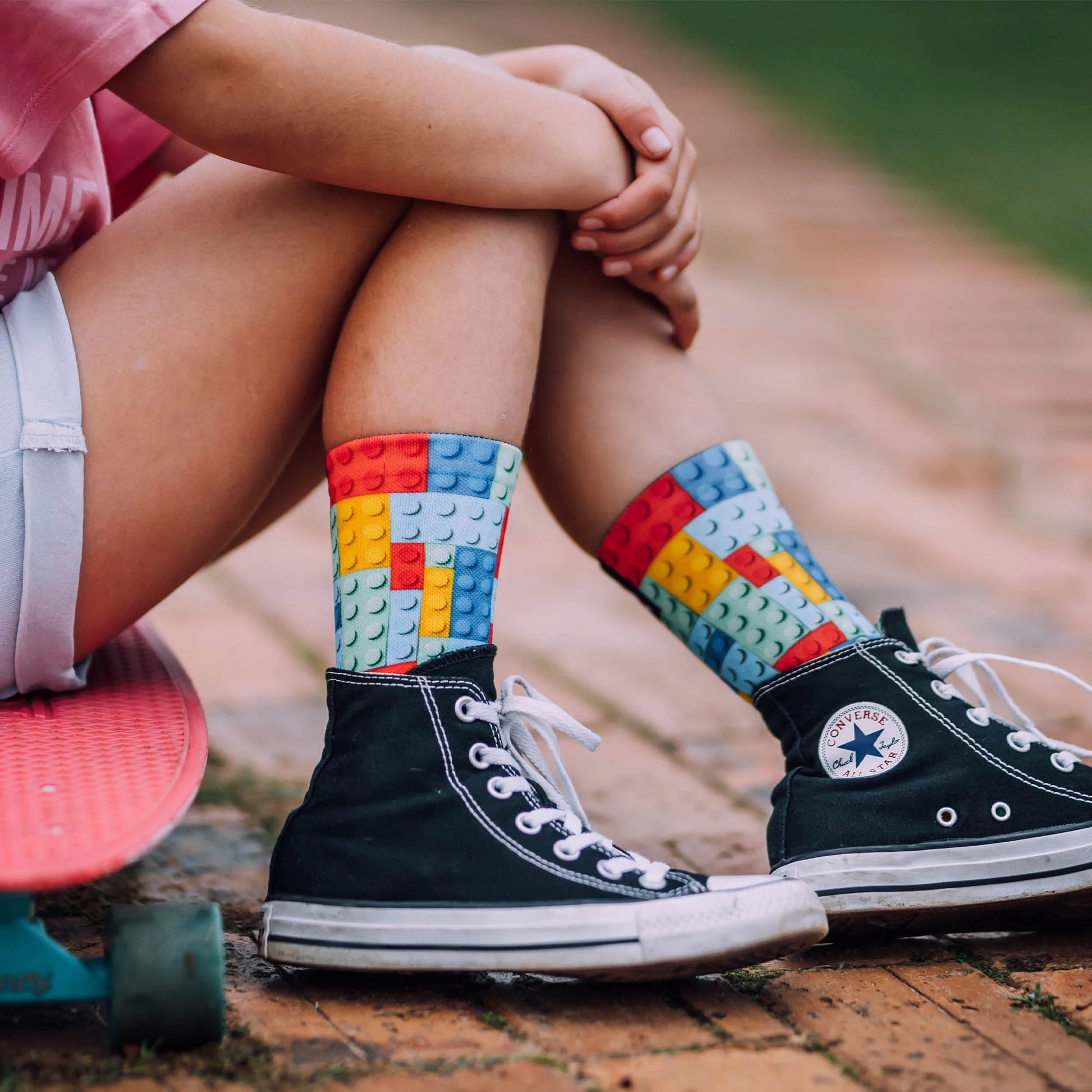 Girl sitting down on skateboard wearing sox footwear, block style.