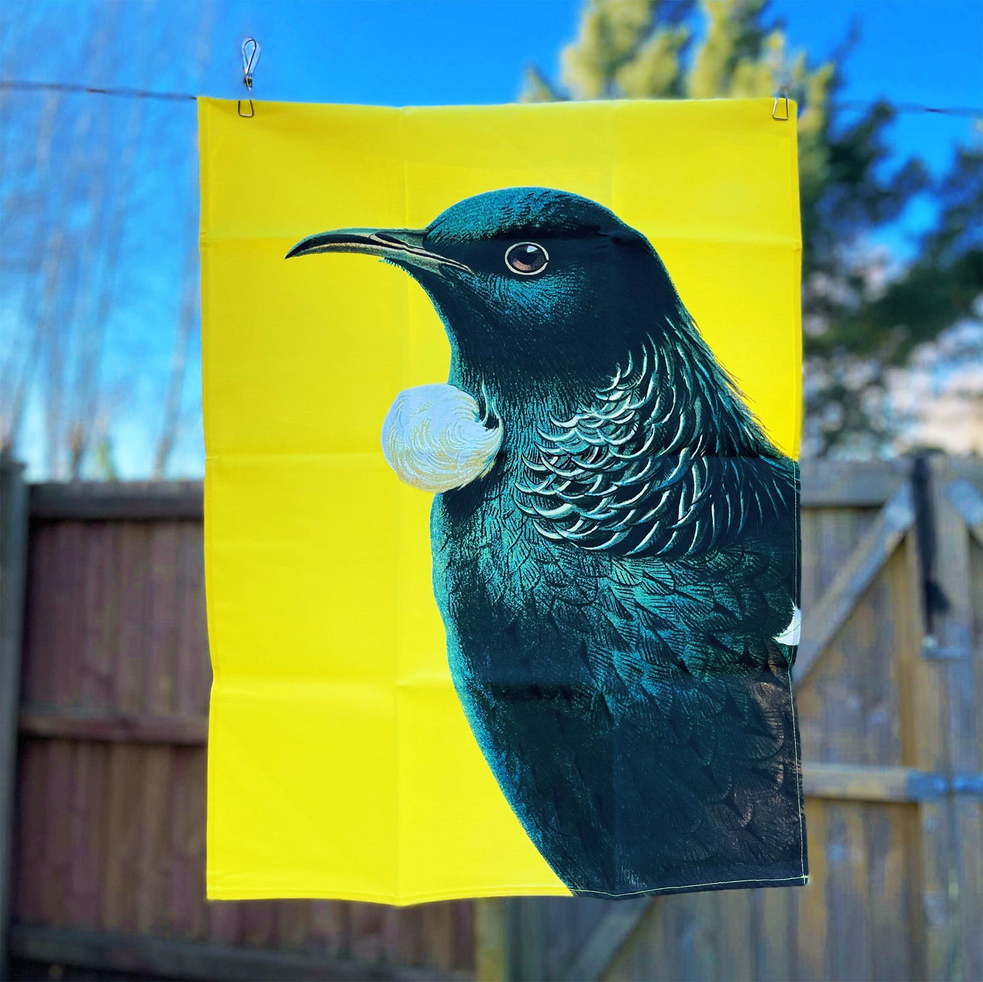 Bright yellow tea towel with a Tui on it.