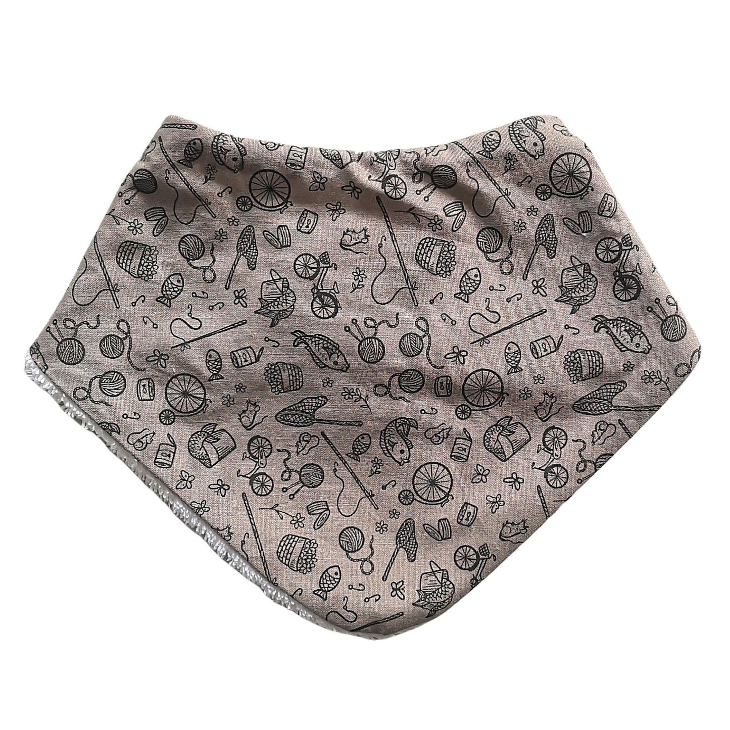 Baby dribble bib in a light mushroom colour with fish, yarn, penny farthings and other little icons in a darker brown print.