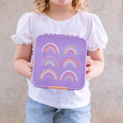 Young child holding a Lilac purple kids lunchbox with pink, peach, white & purple rainbows printed on the lid.