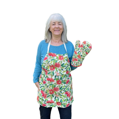 Woman wearing an apron covered in Pohutukawa flower print and showing the matching pot mitt.