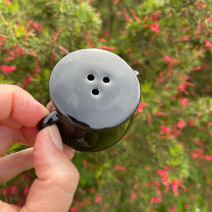 Black ceramic cauldron shaped pepper shaker.