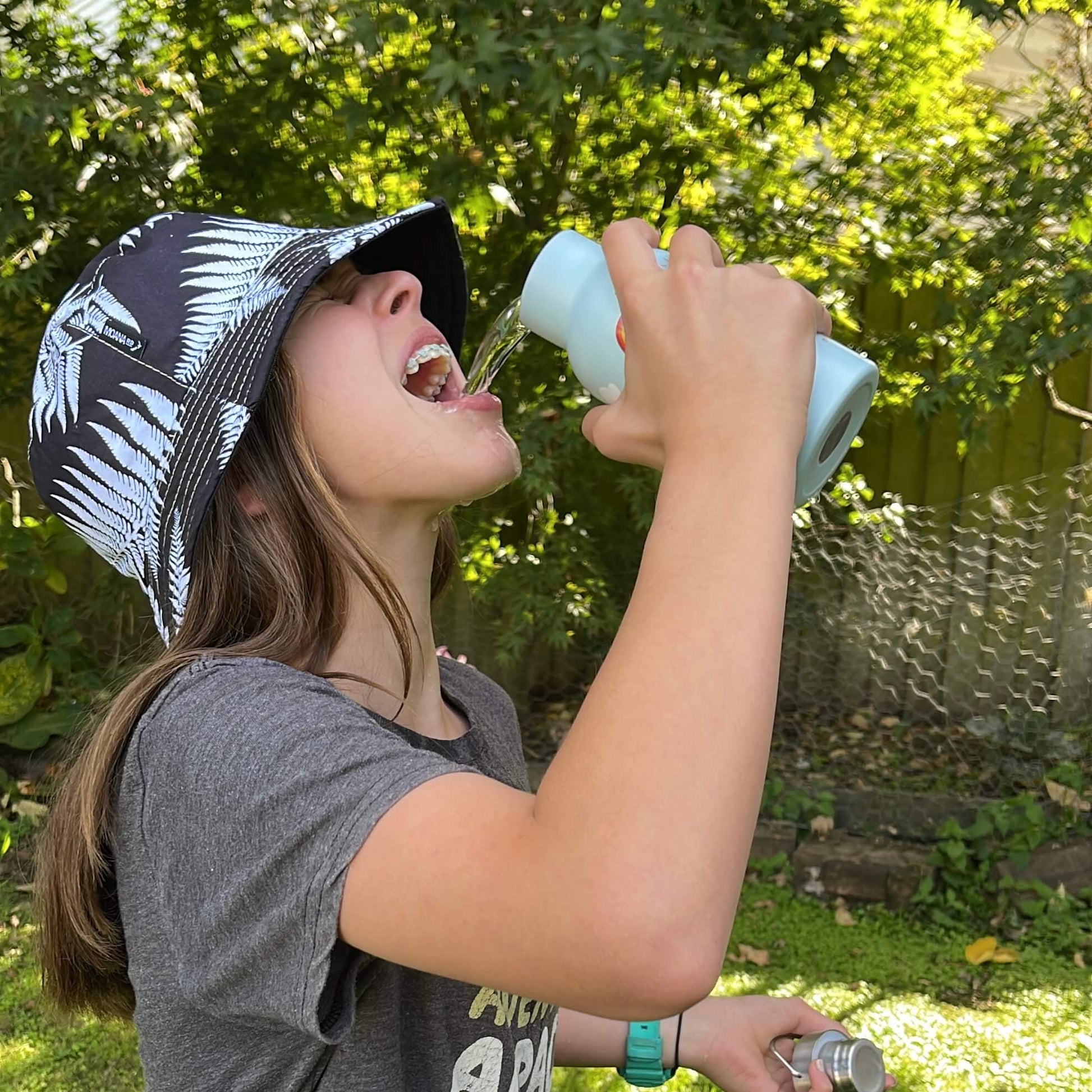 Young girl pouring water from a drink bottle into her mouth.