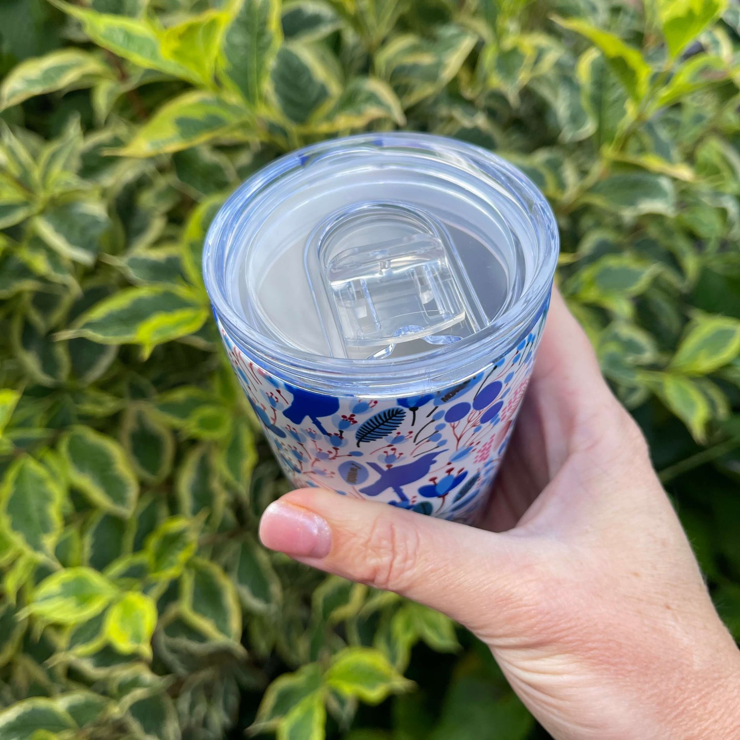 Small reusable coffee cup in white with a blue and red Tui bird and floral design.