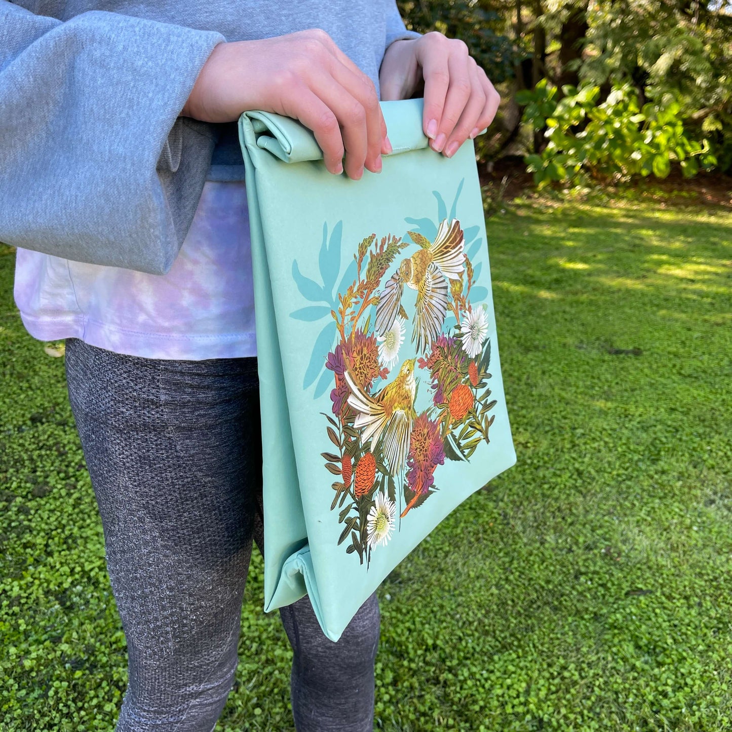 Person holding a light blue folding paper style lunch bag with floral and bird design.