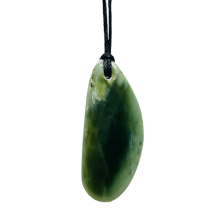 Greenstone freeform pendant on a black wax cord draped over a rock.