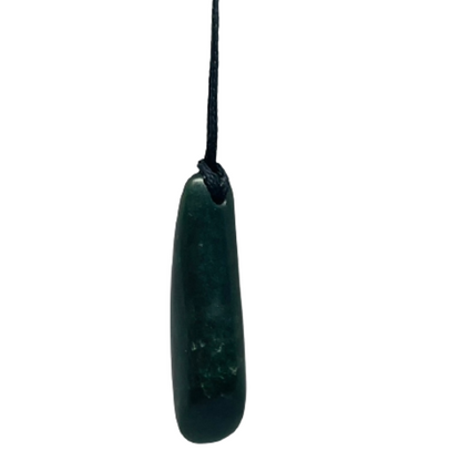 Greenstone freeform pendant on a black wax cord draped over a rock.