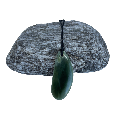 Greenstone freeform pendant on a black wax cord draped over a rock.