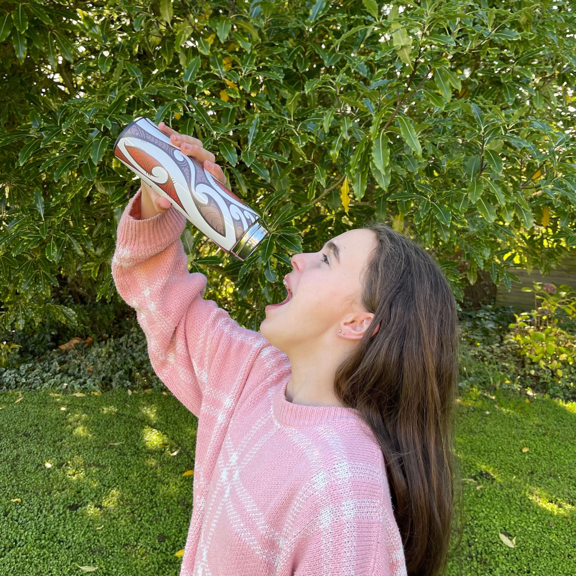 Girl pretending to drink from a Drink bottle with black, white and red koru design.