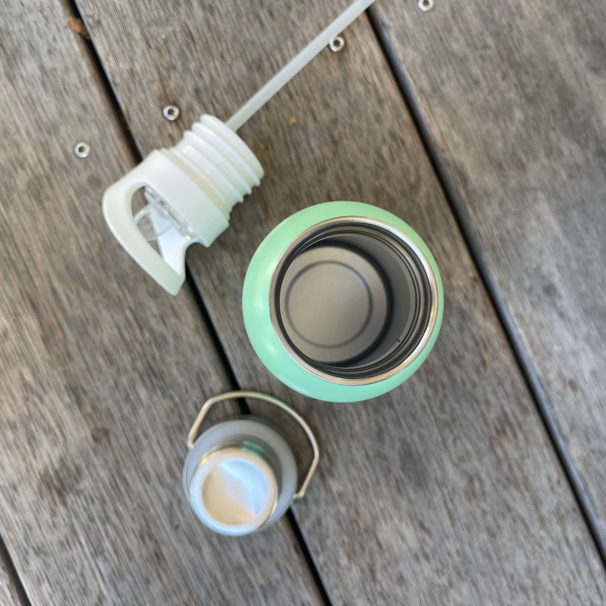 Birds Eye view of double wall drink bottle with two lid options sitting next to it on decking.