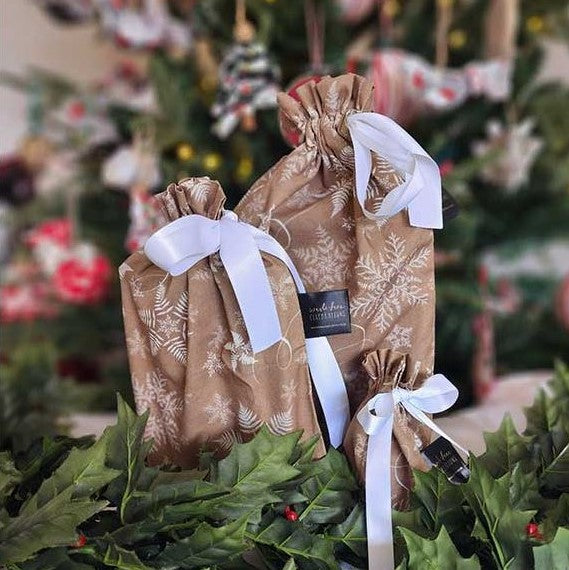 Reusable Christmas gift bags in beige with a white snowflake print and white satin ribbon.